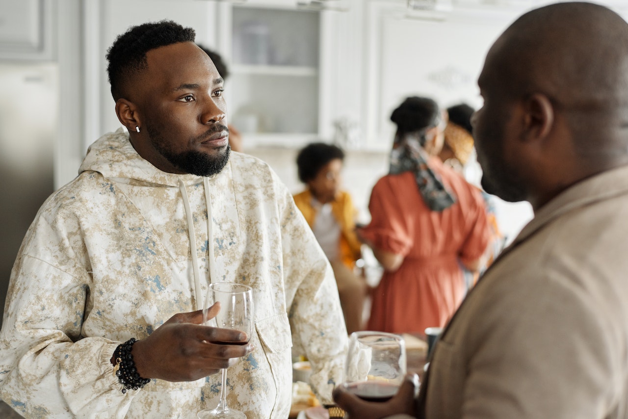 Man wearing white hoodie is talking with other man at party.