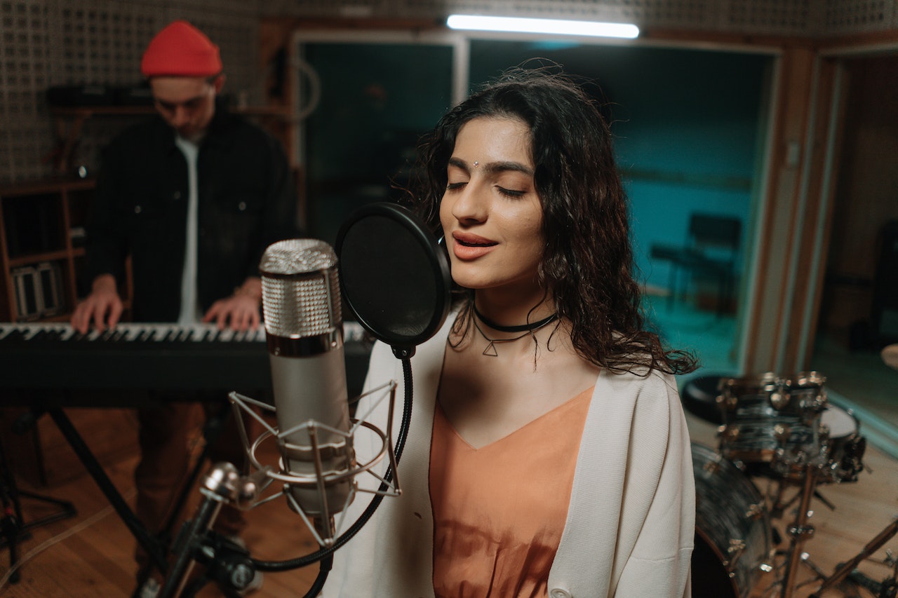 Young woman is singing on microphone in studio.