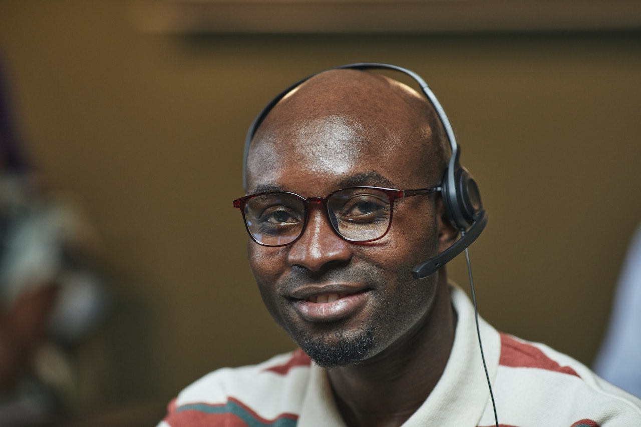 Close up photo of man wearing headset and glasses, smiling at camera.