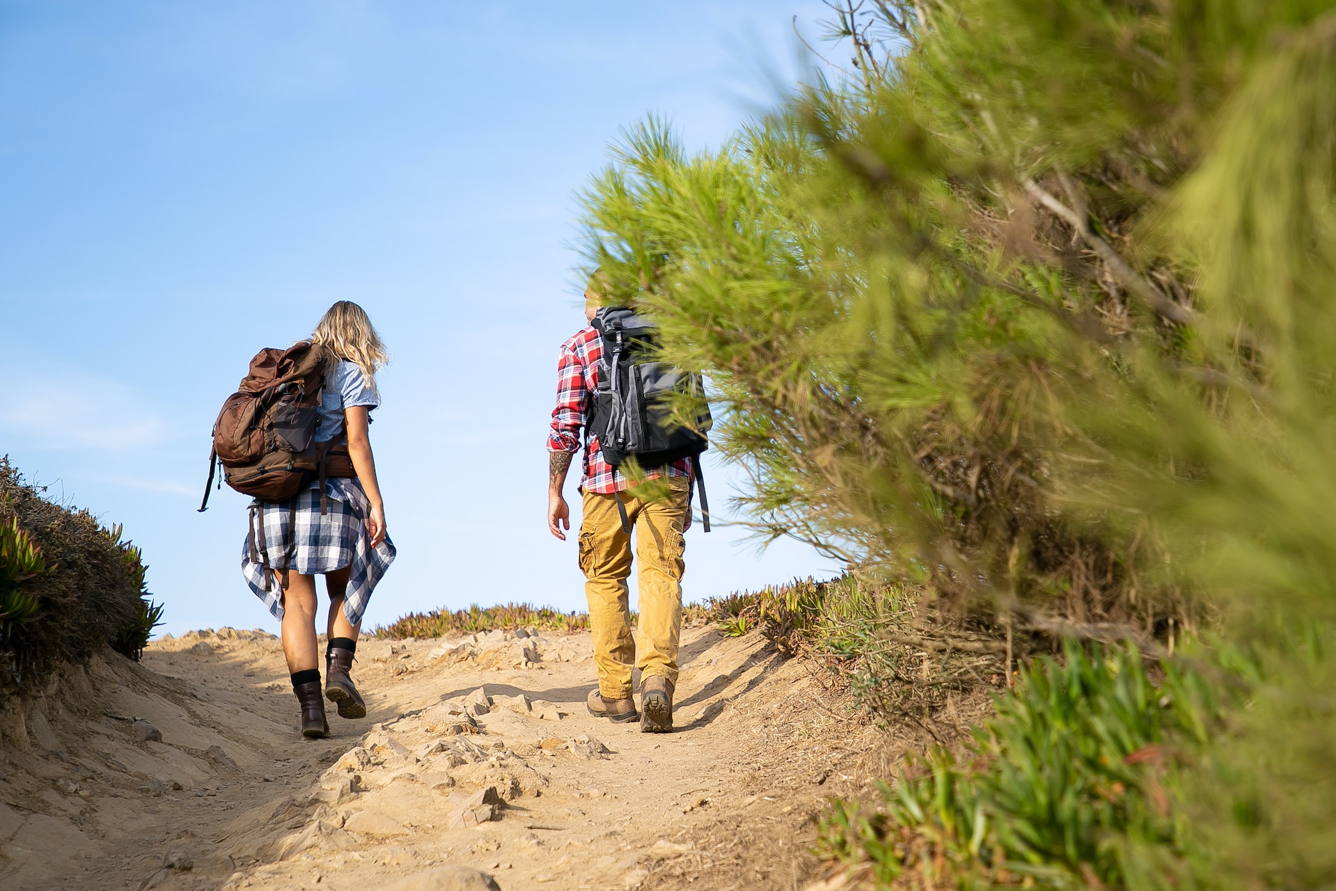 couple hiking up a trail in plaid shirts and backpacks