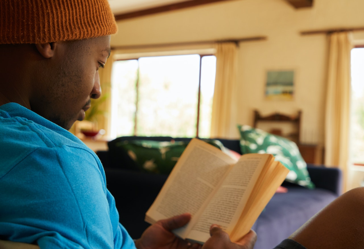 Young man is seating at home and reading a book.