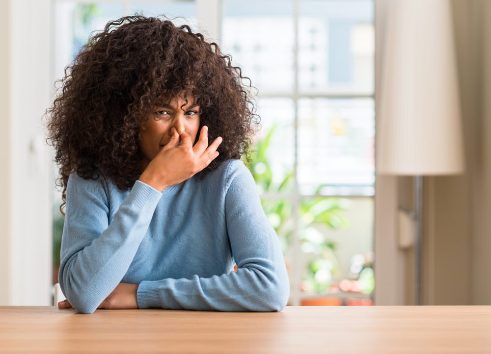 woman in blue sweater  at home smelling something stinky