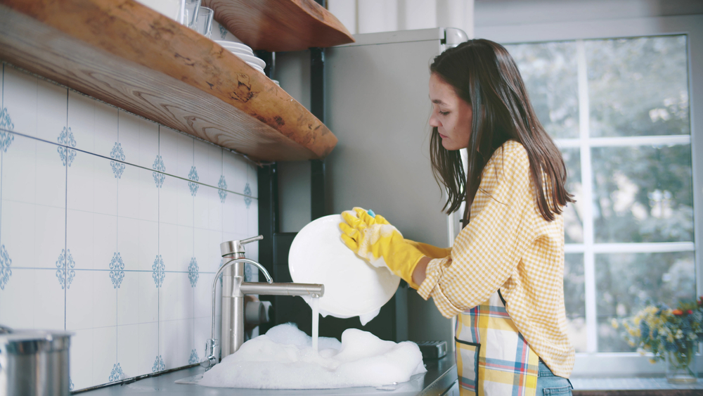 woman in apron and gloves washing dishes