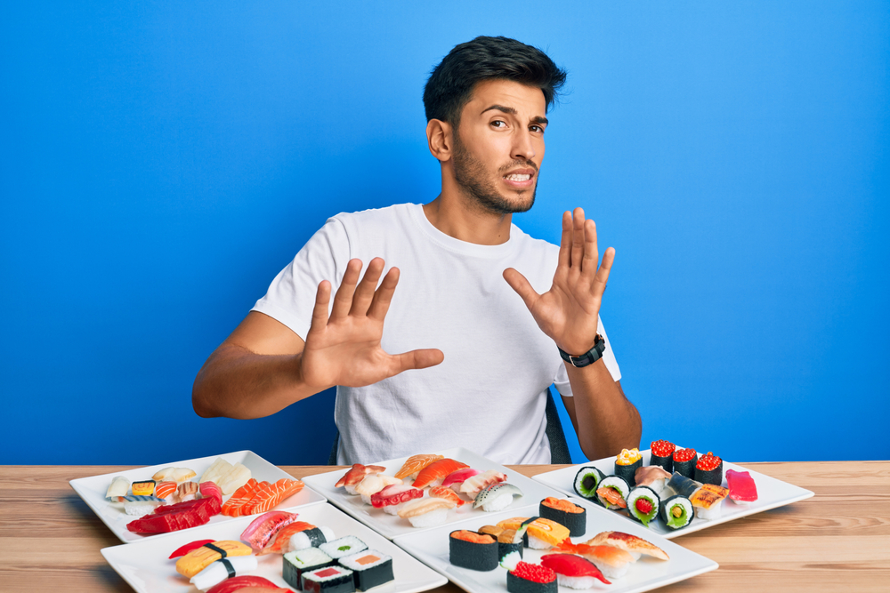 Young handsome man disgusted from  eating sushi sitting on a table