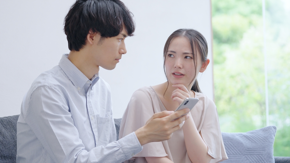 Angry Asian young couple looking at a smartphone arguing
