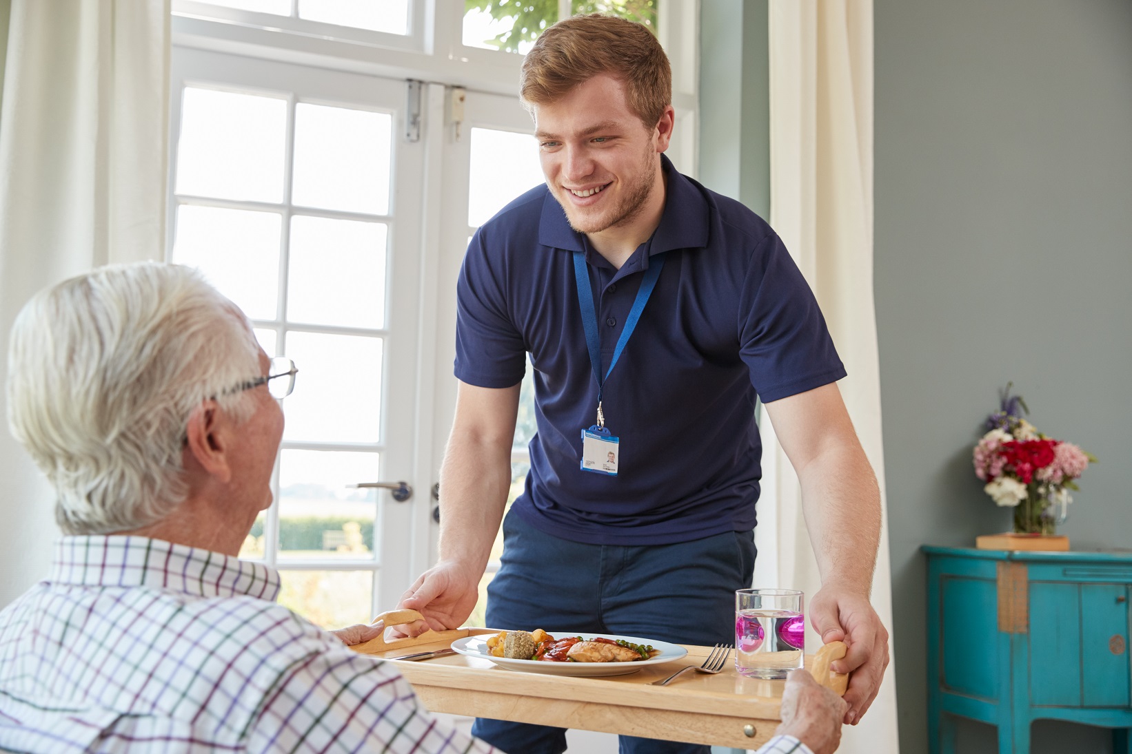Male care worker serving dinner to a senior man and smiling at nursing home.