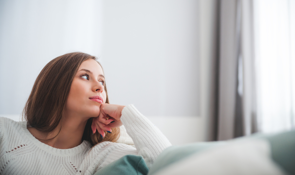Sad woman sitting on sofa at home deep in thoughts, thinking about someone