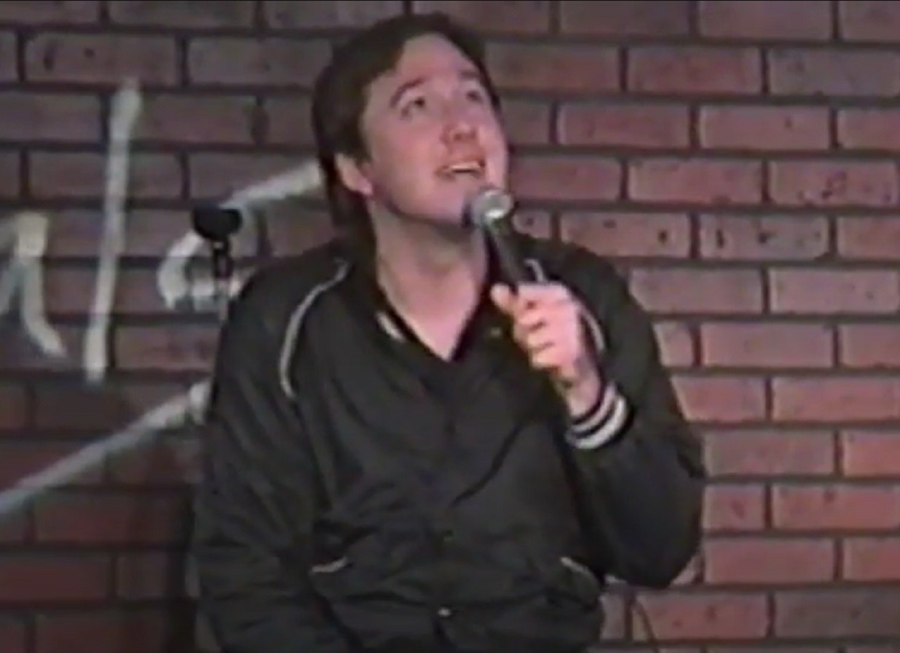 Screenshot: Bill Hicks wearing black shirt is looking up on stage - from American- The Bill Hicks Story (2009)
