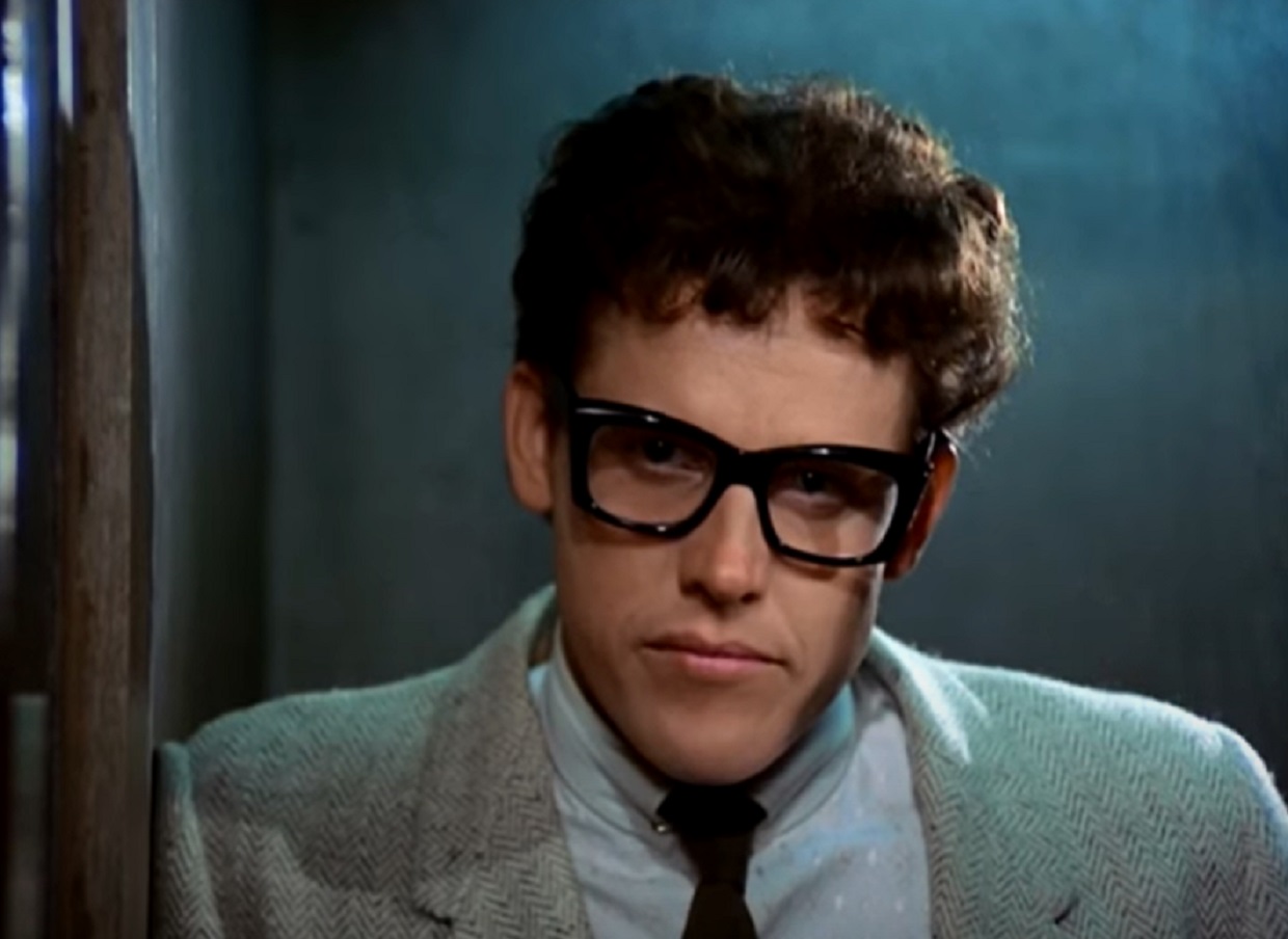 Screenshot: Buddy Holly wearing grey suit and black glasses  - from The Buddy Holly Story (1978).