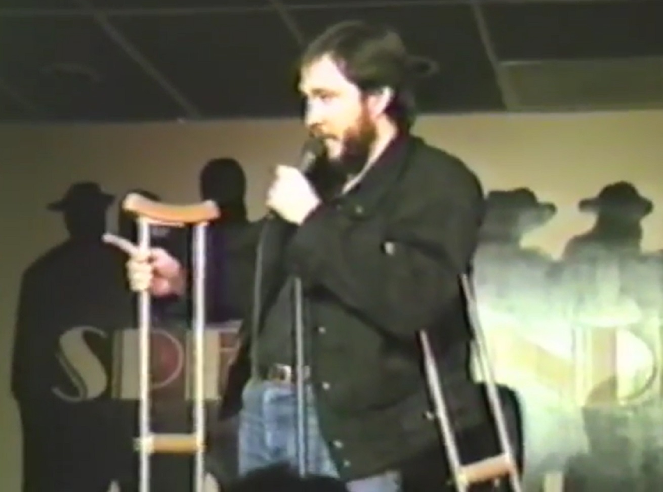 Screenshot: Bill Hicks is performing on stage with injured leg - from  American- The Bill Hicks Story (2009)