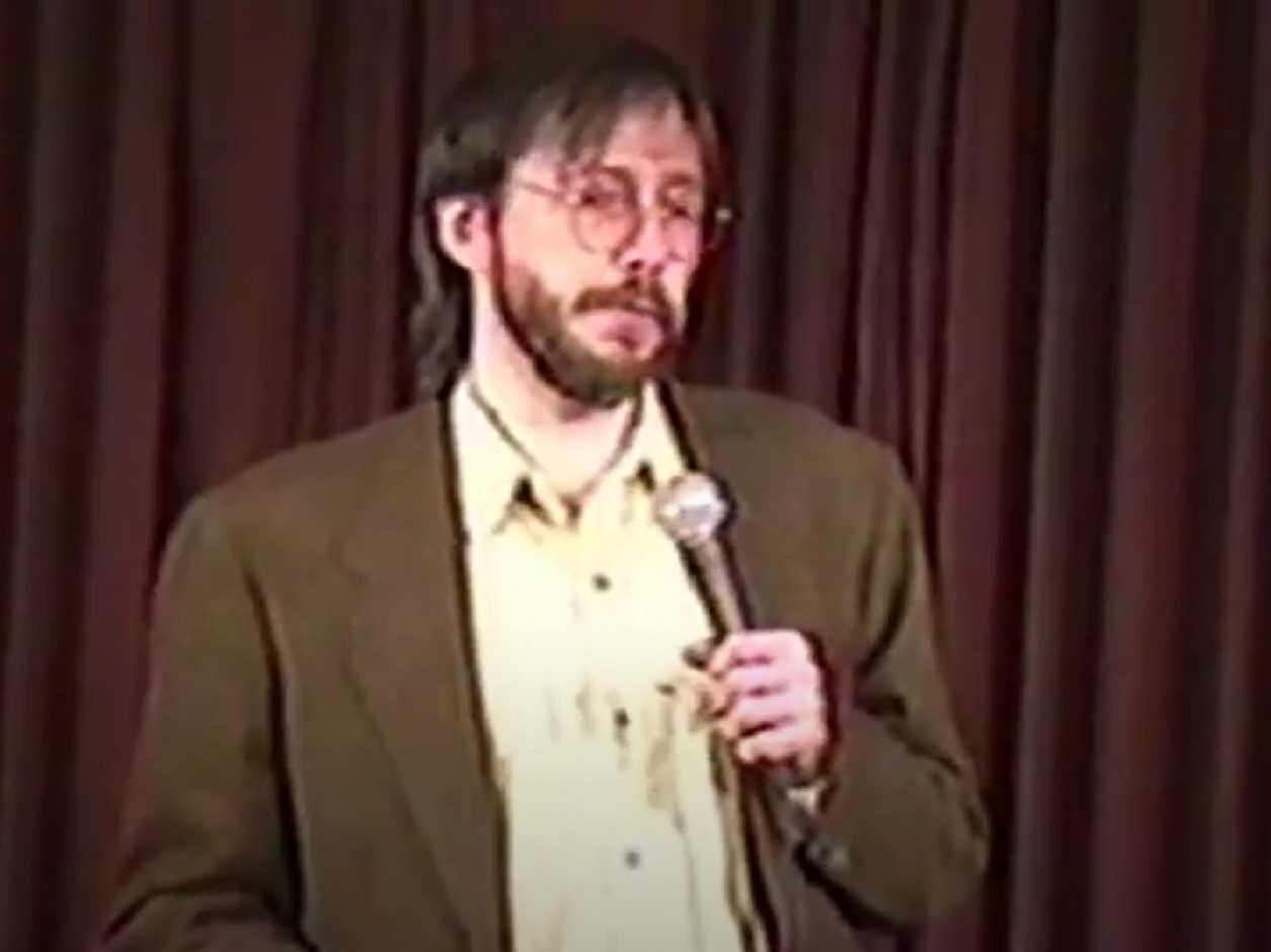 Screenshot: Bill Hicks with beard is performing on stage - from American- The Bill Hicks Story (2009)
