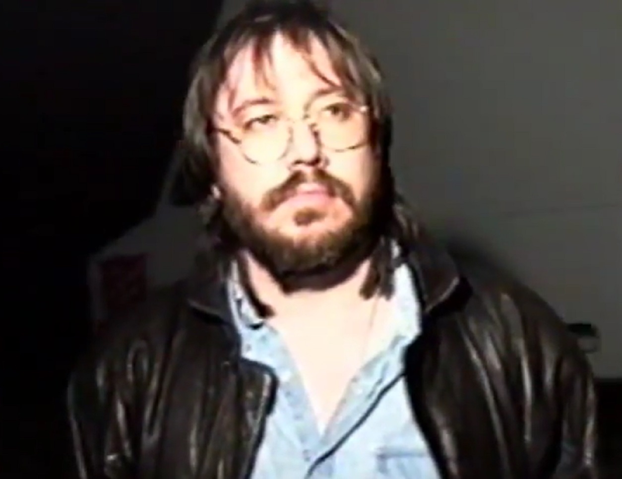 Screenshot: Bill Hicks wearing blue shirt and black jacket is looking at side - from American- The Bill Hicks Story (2009)