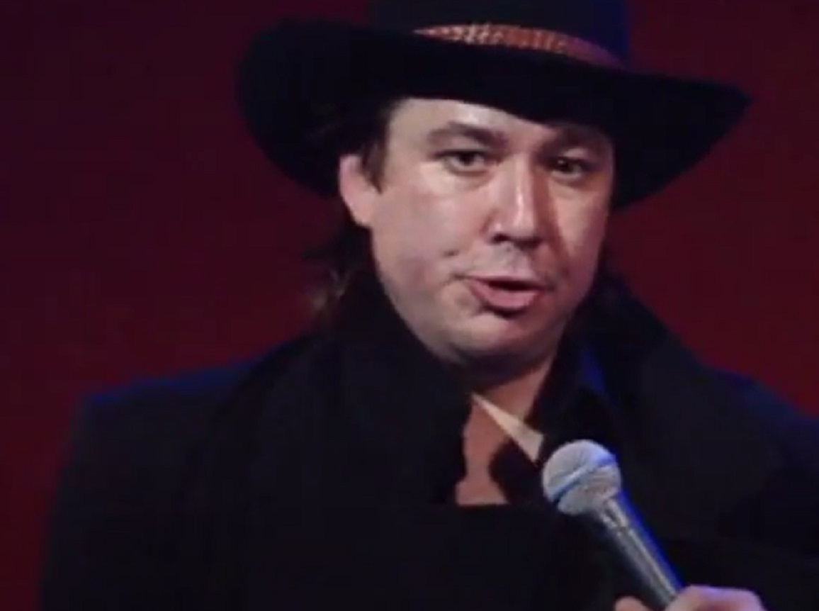 Screenshot: Bill Hicks is looking at side and talking on stage - from American- The Bill Hicks Story (2009)