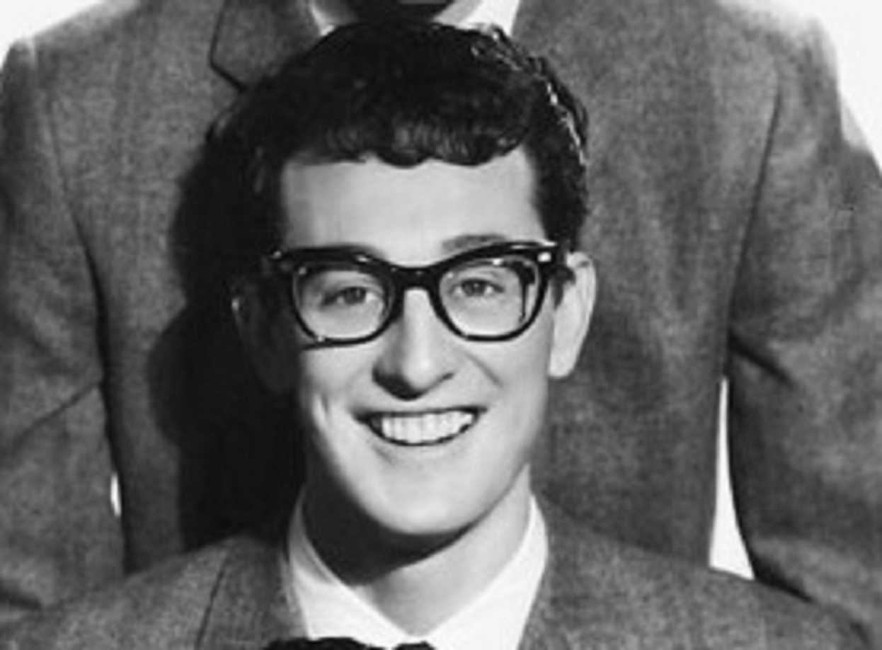 Buddy Holly wearing suit and glasses is smiling at camera - circa 1957-58