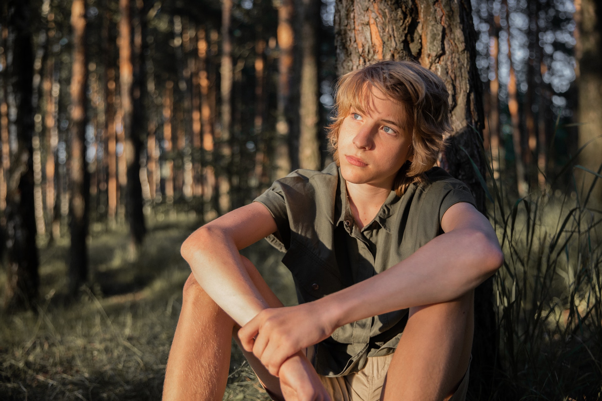 Boy in Khaki T-Shirt Sitting on the Ground Beside the Tree