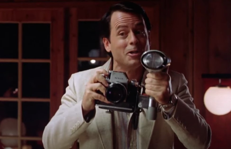 Greg Kinnear  as  Bob Crane in white jacket taking a photo