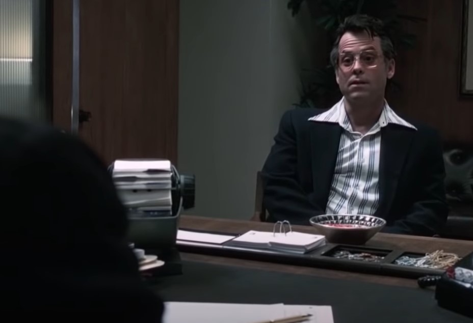 Greg Kinnear  as  Bob Crane in suit sitting on a chair