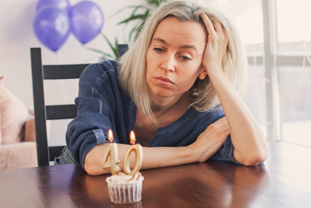 Sad lonely woman is sitting at table and looking at birthday cake for her  40th birthday