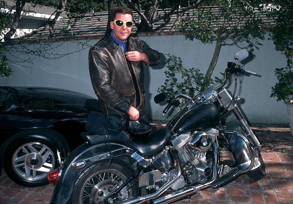 Judd Nelson behind a motorcycle in leather jacket and glasses