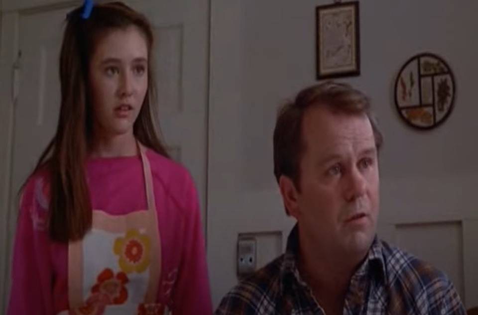 Shannen Doherty in Girls Just Want to Have Fun wearing pink sweater and apron looking shocked
