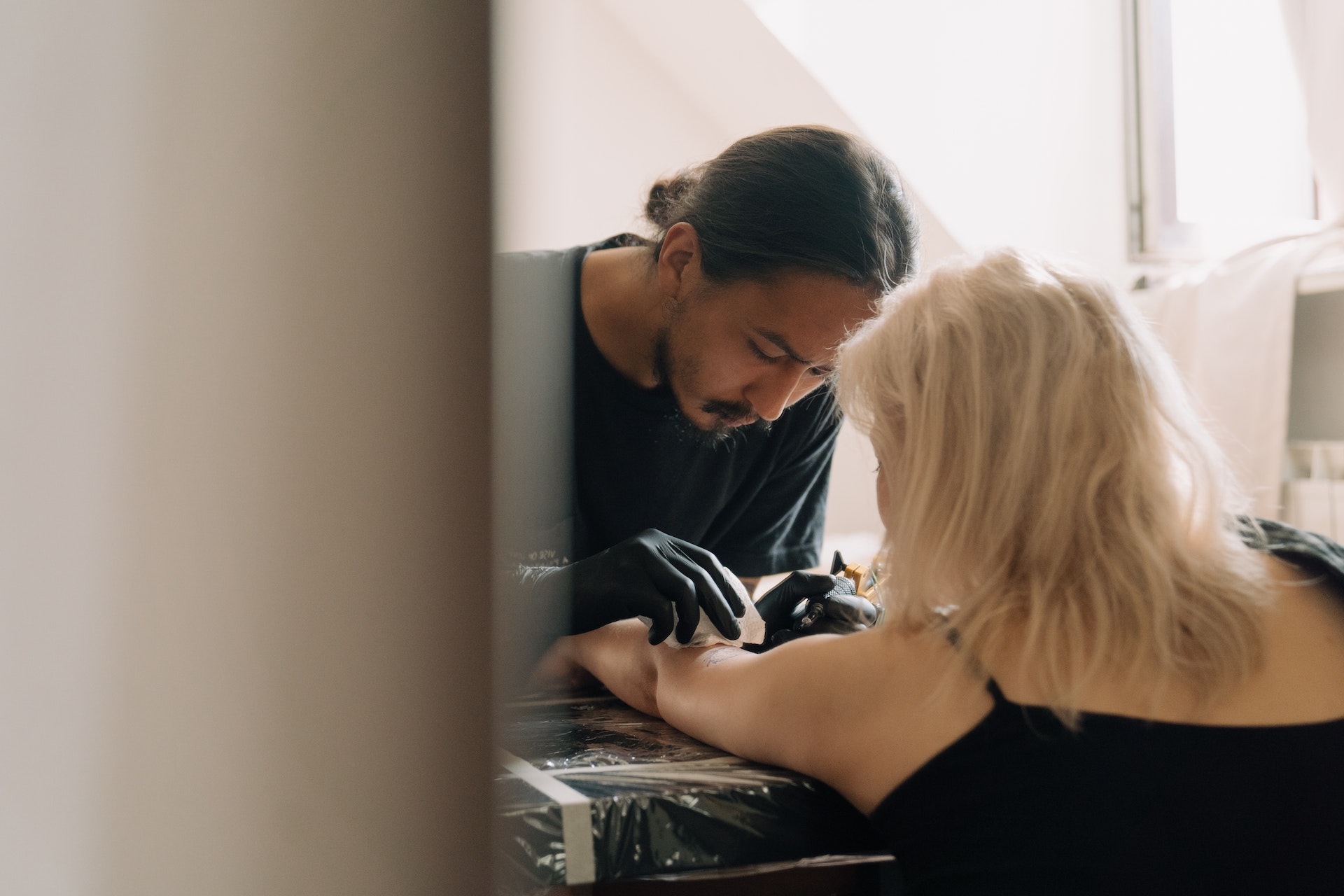 Tattoo artist doing a tattoo on a woman in black top