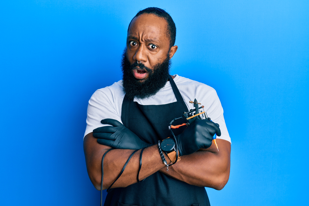 Young African American man tattoo artist wearing professional uniform and gloves holding tattoo machine