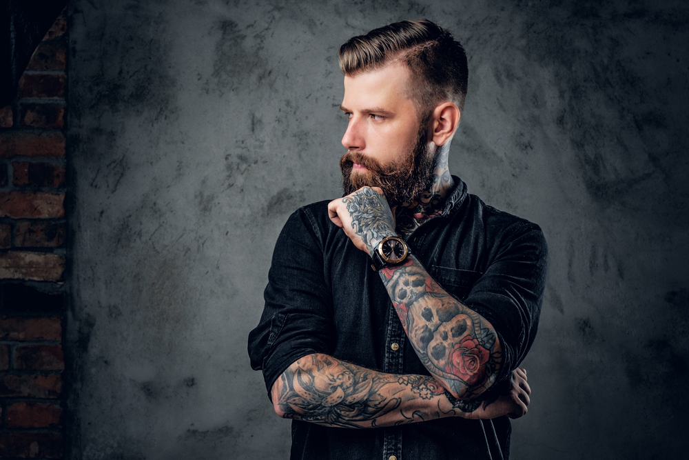 Portrait of bearded hipster tattoo artist in black shirt with tattoos on his arms