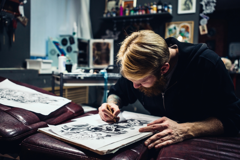 Adult male artist draws a tattoo in blue sweatshirt