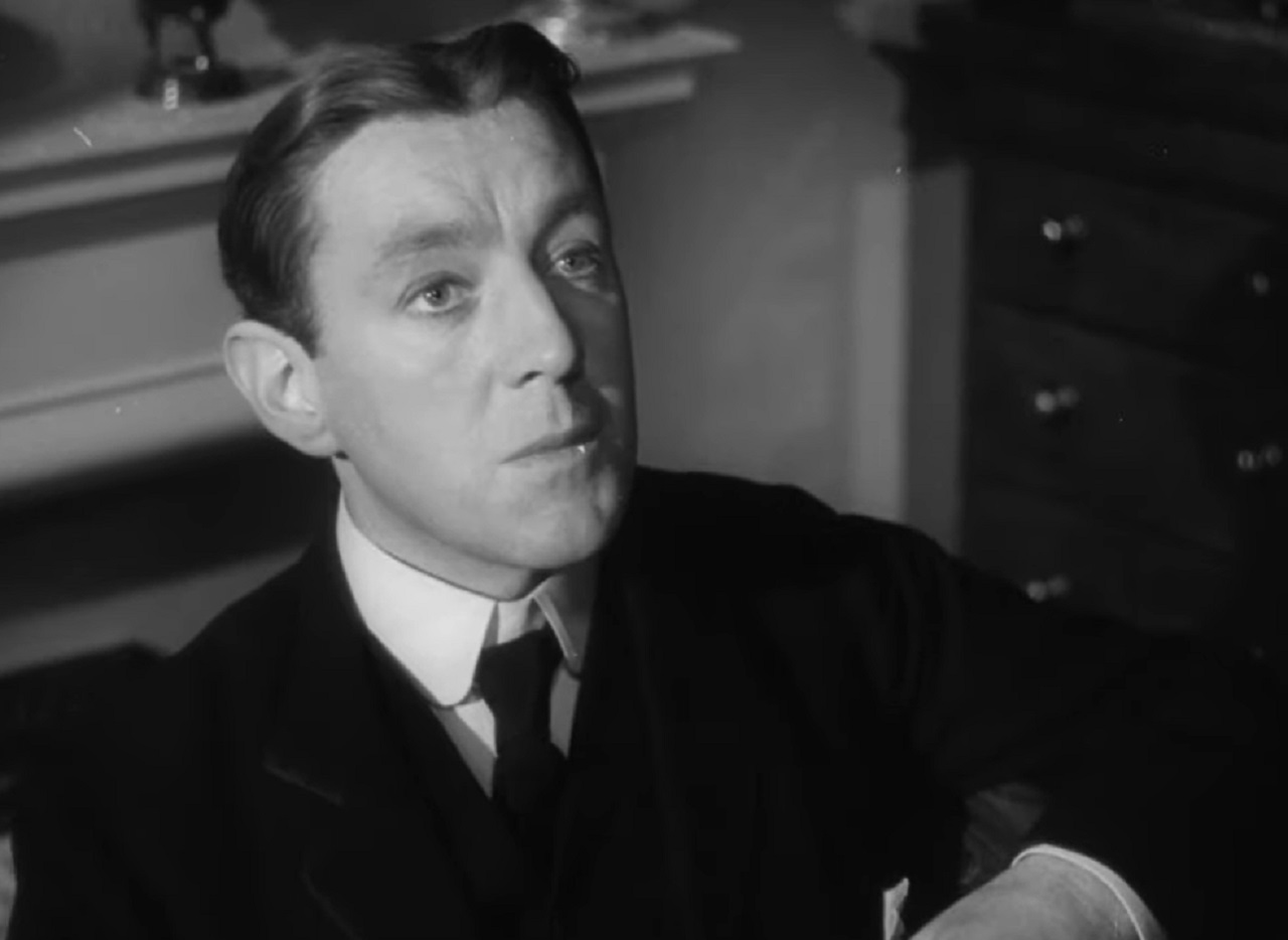 Screenshot of Alec Guinness wearing suit and looking at side - from The Promoter (1952)