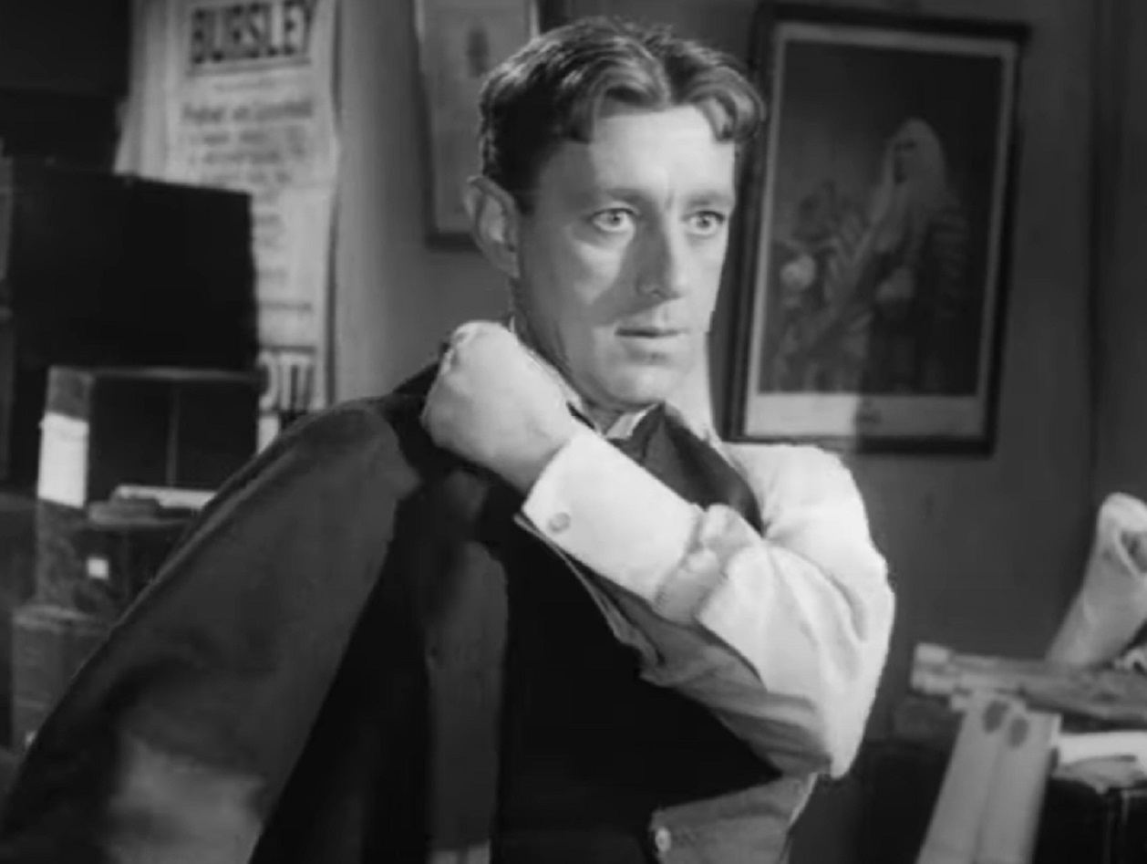 Screenshot of Alec Guinness wearing black jacket and looking at front - from The Promoter (1952)