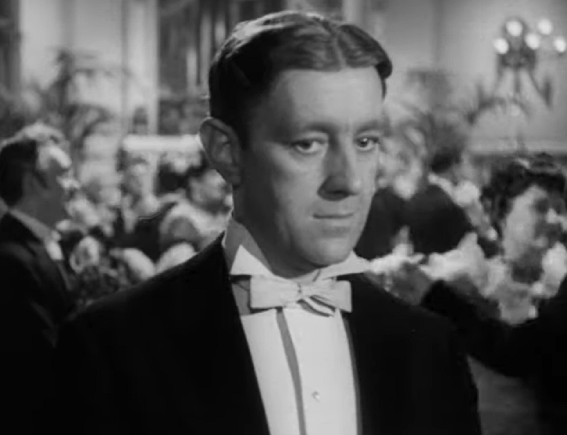 Screenshot of Alec Guinness wearing suit and looking at side - from The Promoter (1952)