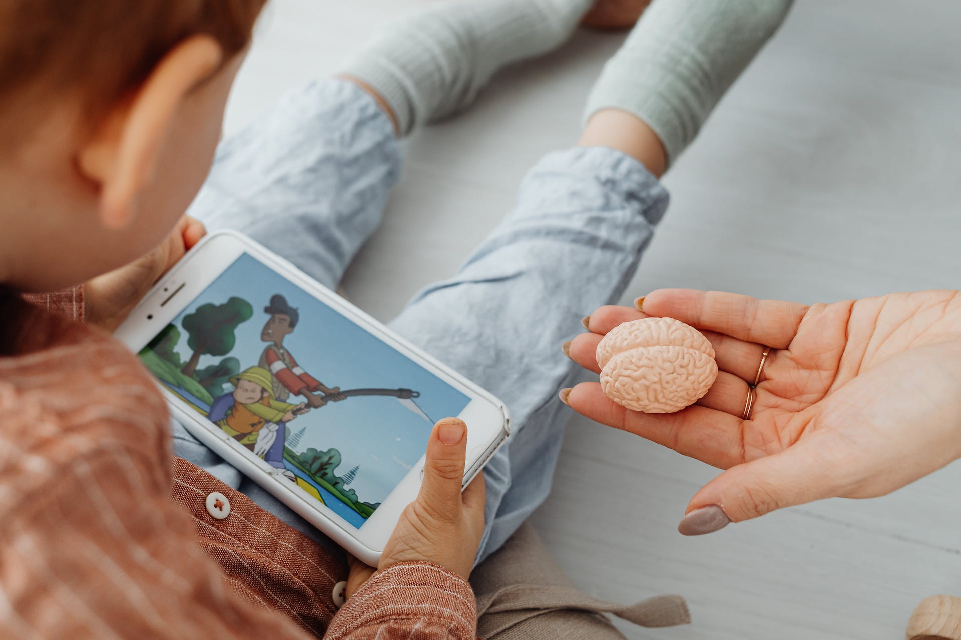 photo of a kid watching on a cell phone and a woman hand showing little human brain model