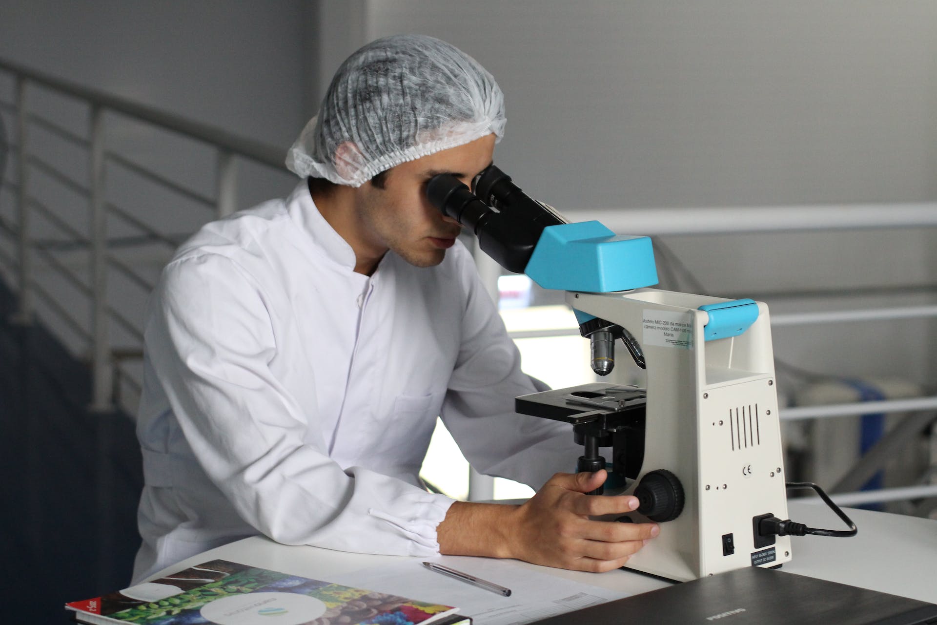 photo of a scientist in a white outfit looking in to the microscope