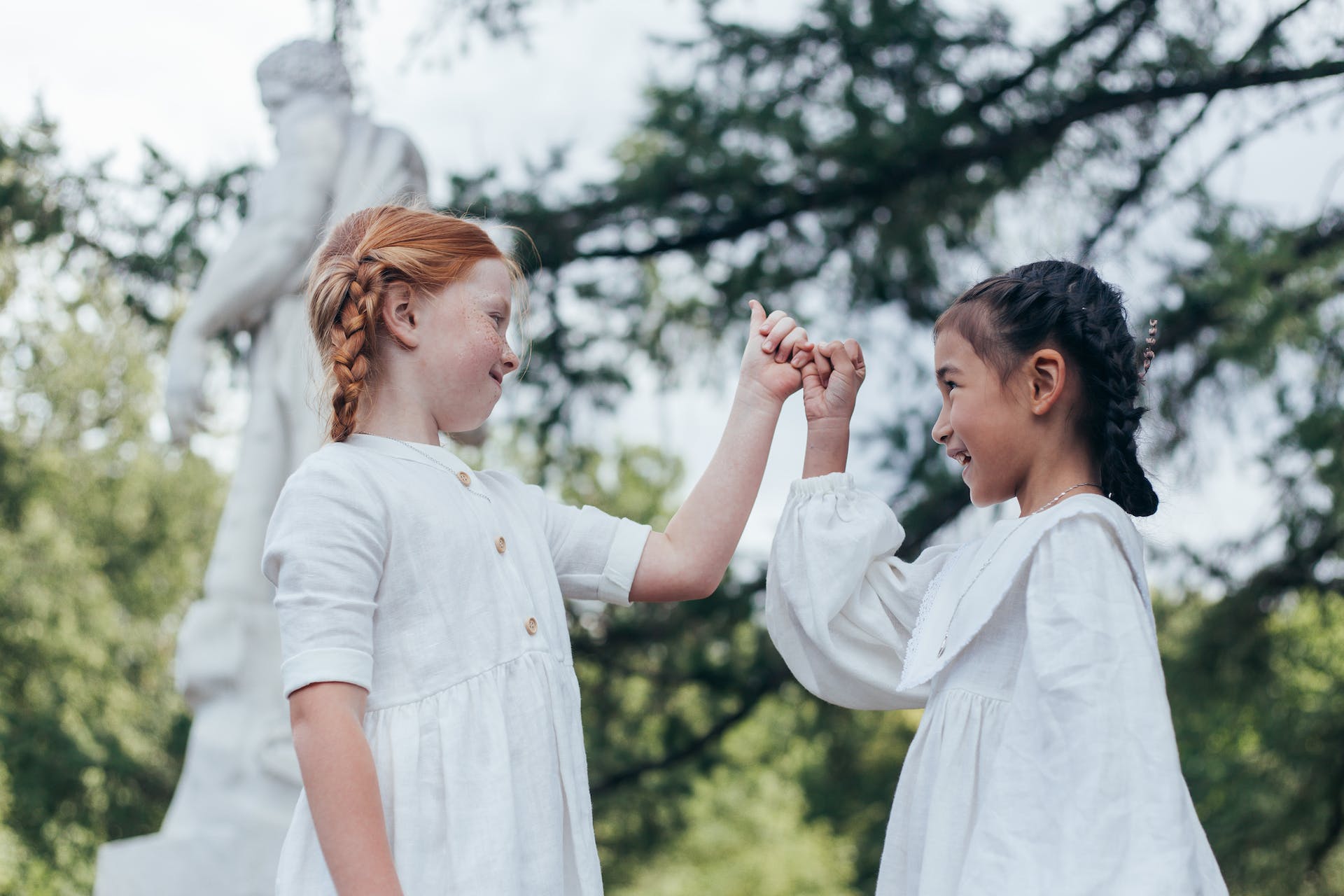two young friends in white dresses doing pinky promise
