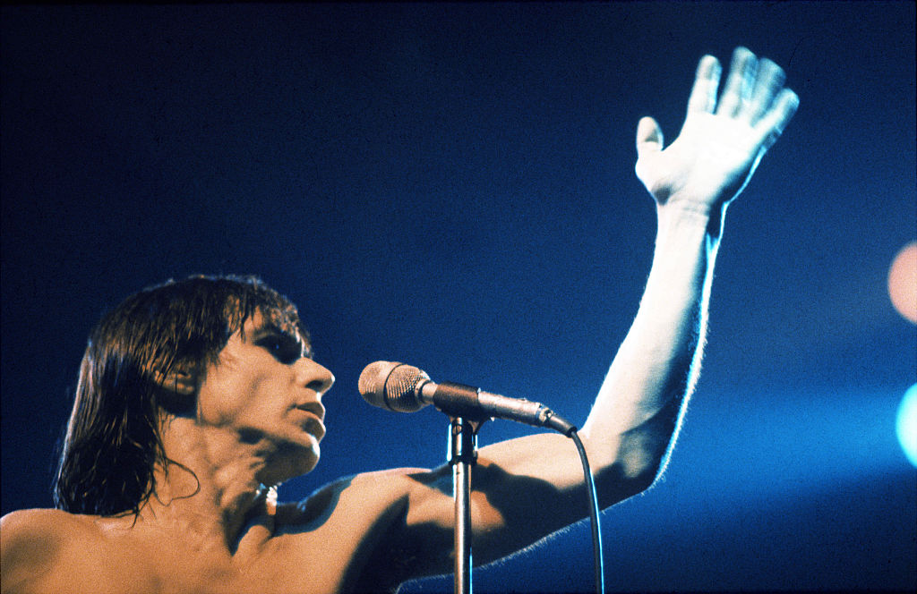 Iggy Pop performs on stage in Aylesbury  facing right with raised hand