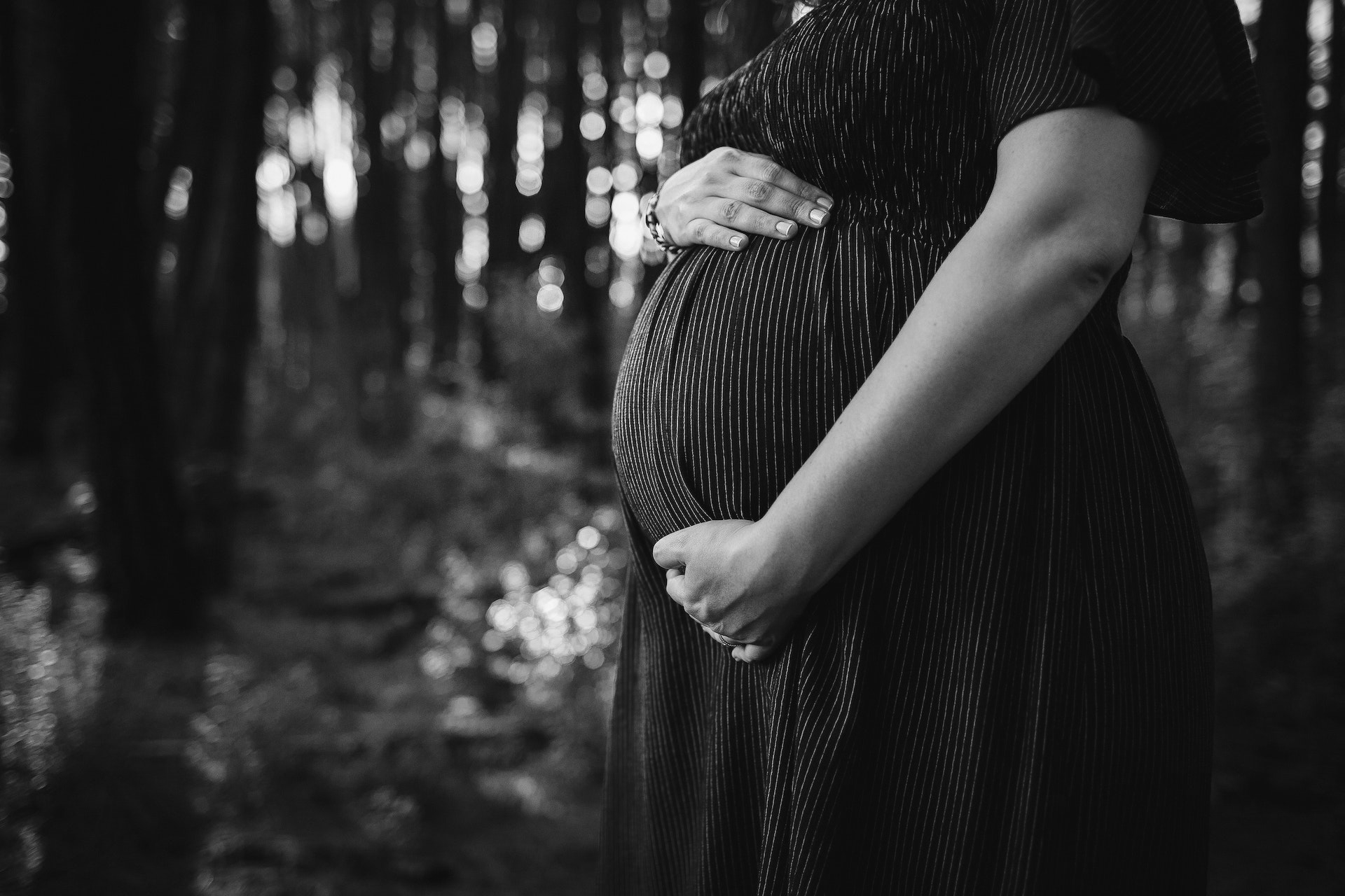 Pregnant woman embracing belly while standing in forest