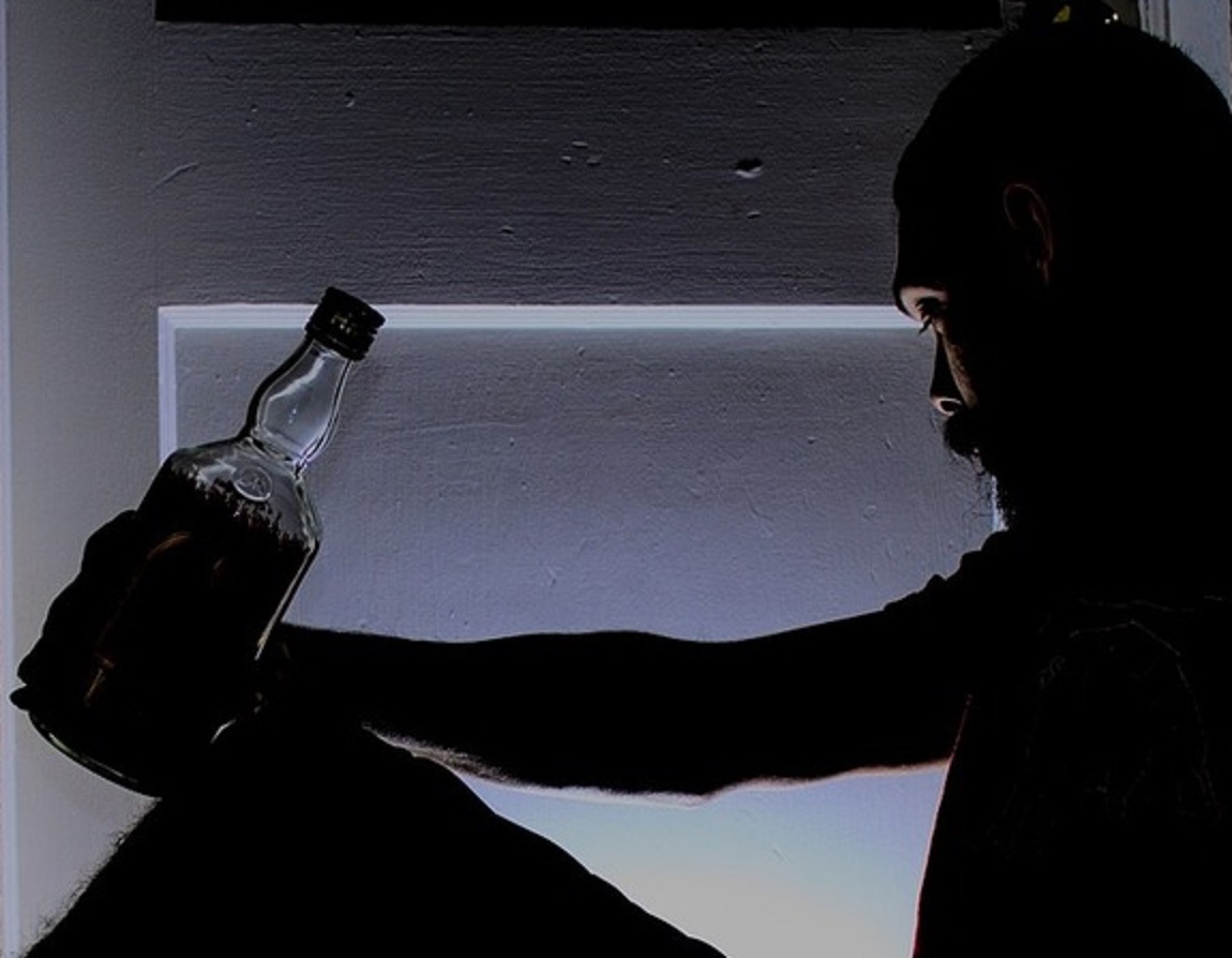 A man sitting on a floor holding a bottle