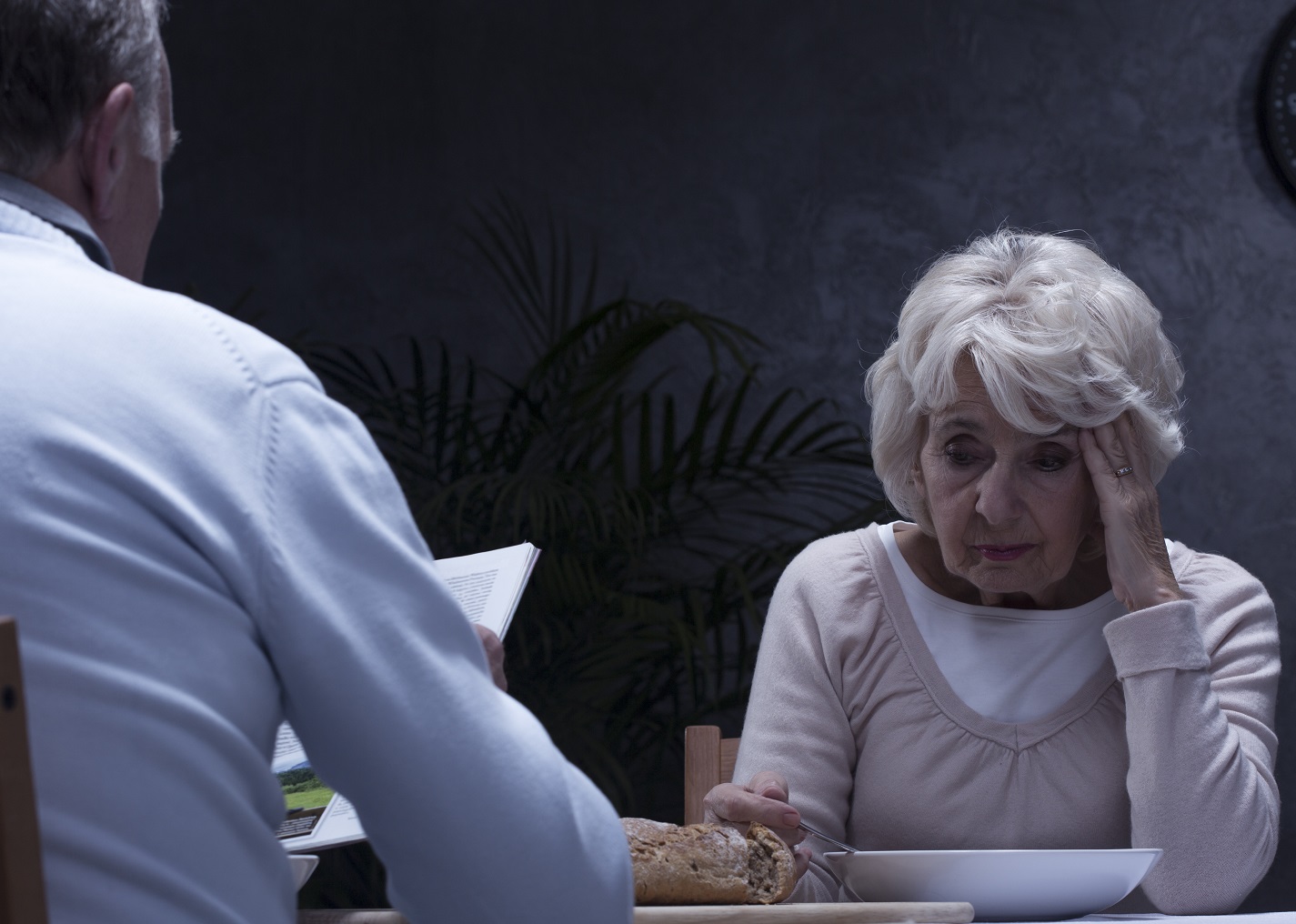 Shot of an elderly couple sitting at the table in a dark living room