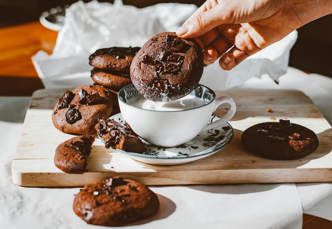 Person Holding Chocolate Chip Cookies near Cup of Milk