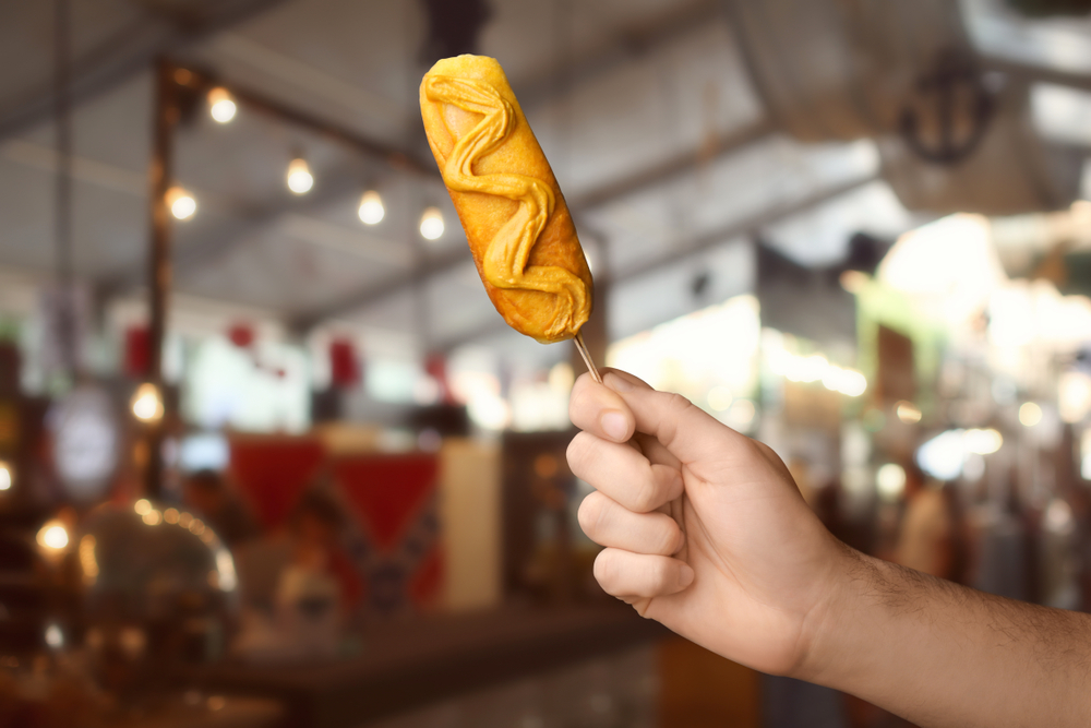 Man holding tasty corn dog with mustard.