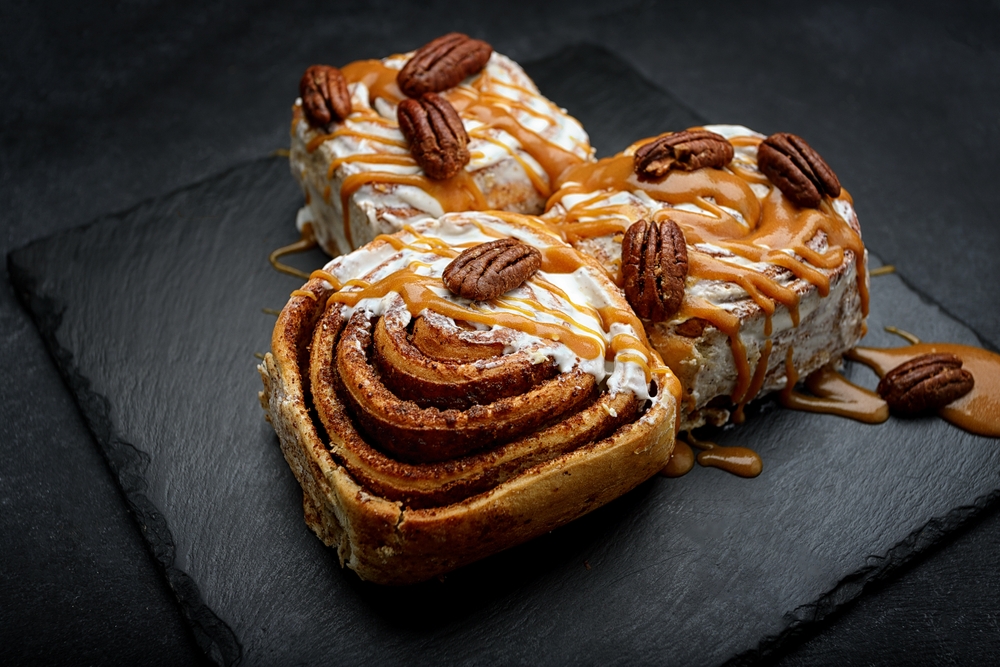 Cinnabon buns with cinnamon, cream, nougat and nuts, on a dark background