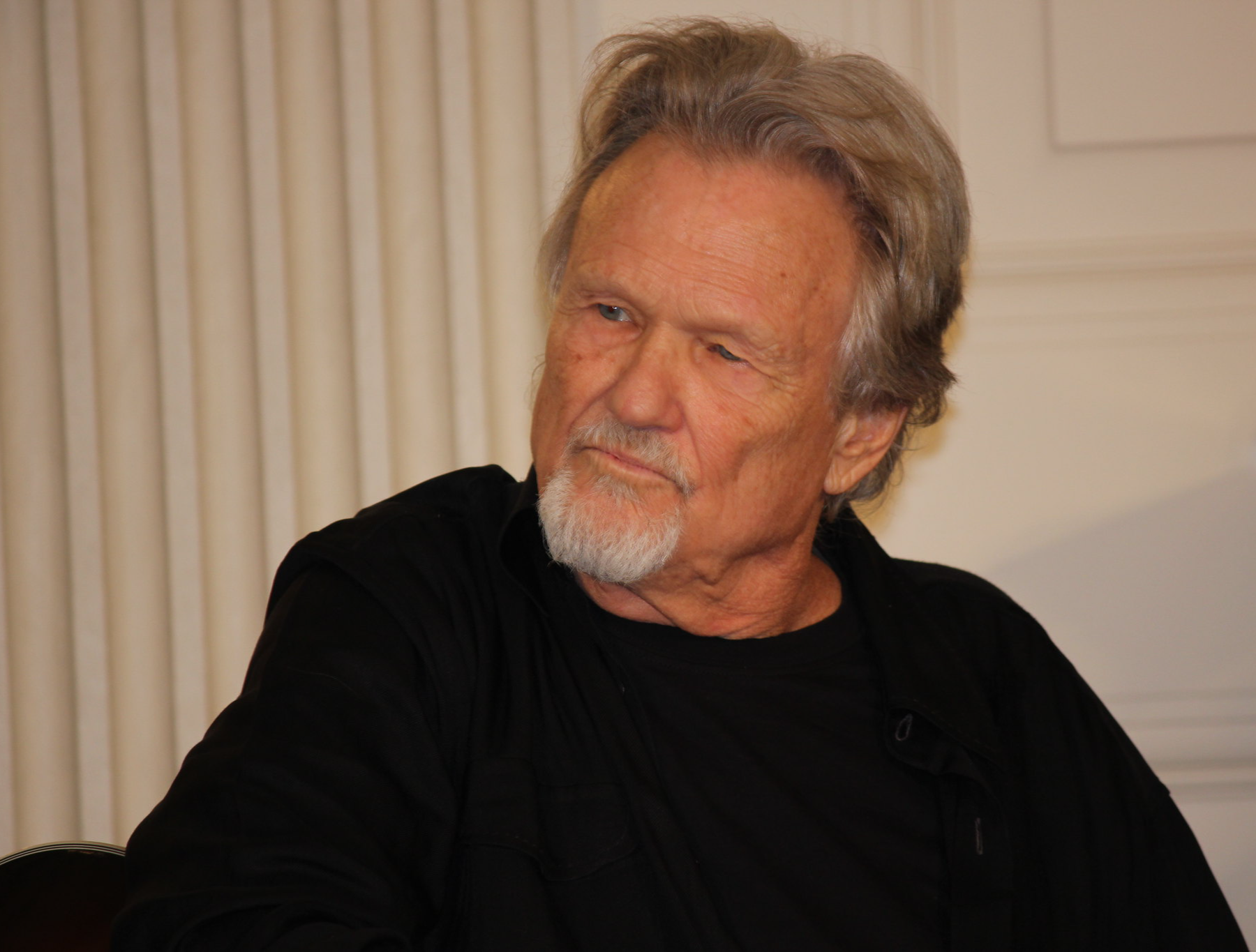 Kris Kristofferson looking at side in black shirt.