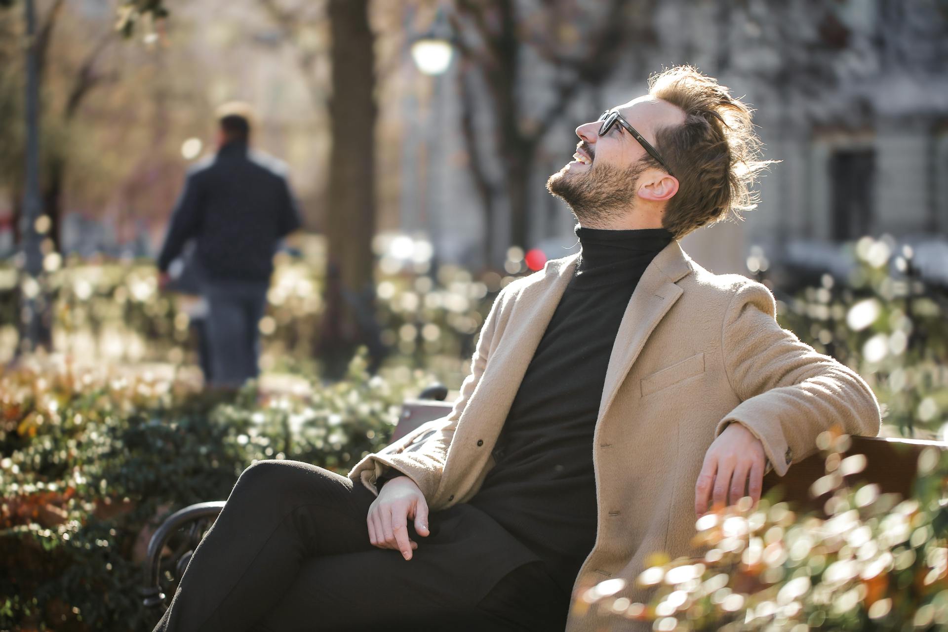 Man in beige coat and glasses sitting on a bench