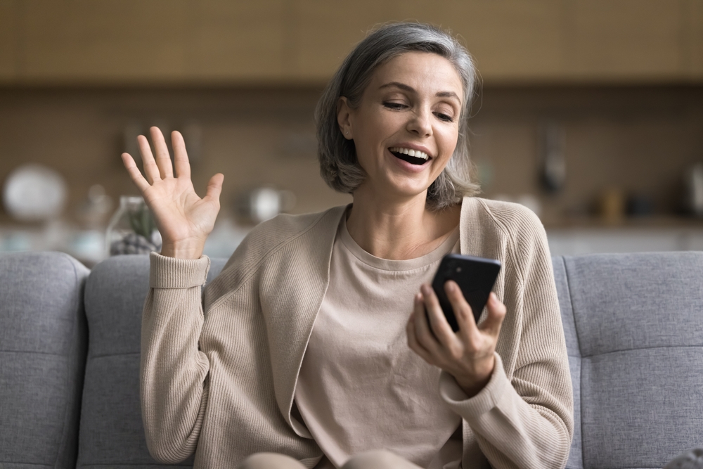 Happy middle-aged woman sitting on sofa holding mobile phone