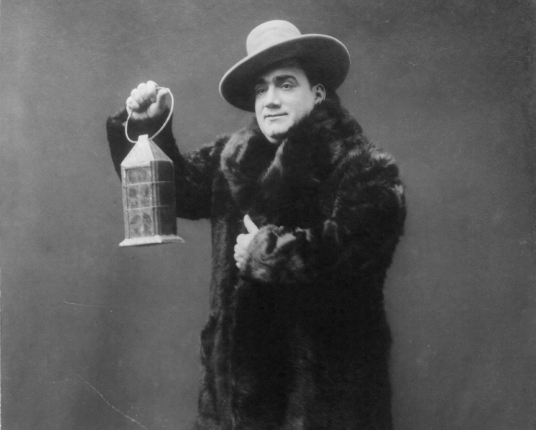 Enrico Caruso, full-length portrait, standing, facing left, wearing fur coat and holding lantern - 1911