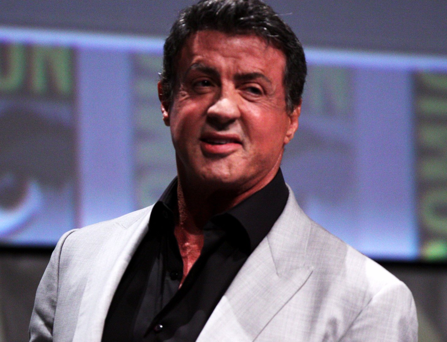 Sylvester Stallone wearing a black shirt and a grey jacket
