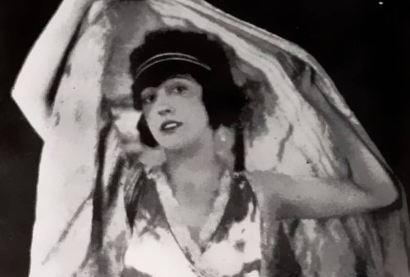 Mabel Normand in shiny dress cowering her head with a scarf