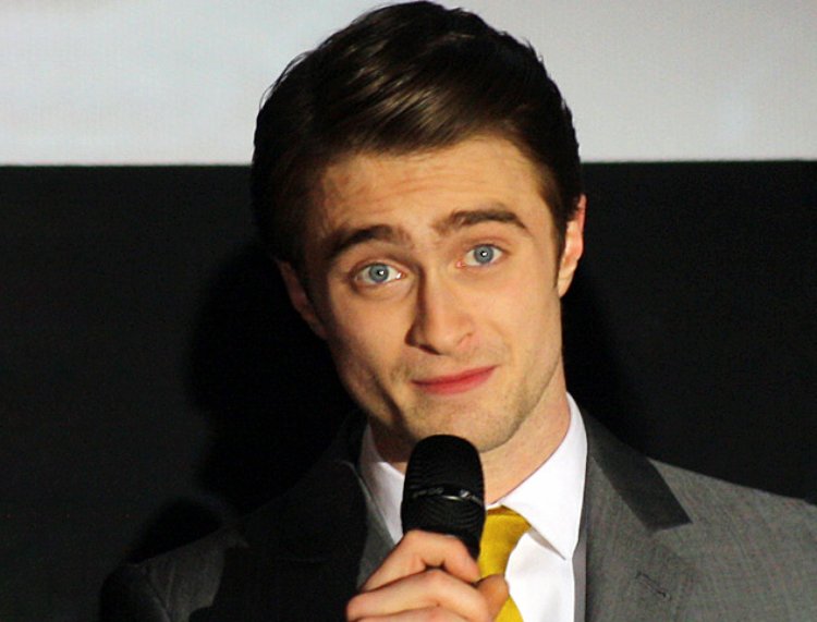 Daniel Radcliffe wearing a grey jacket and holding a microphone