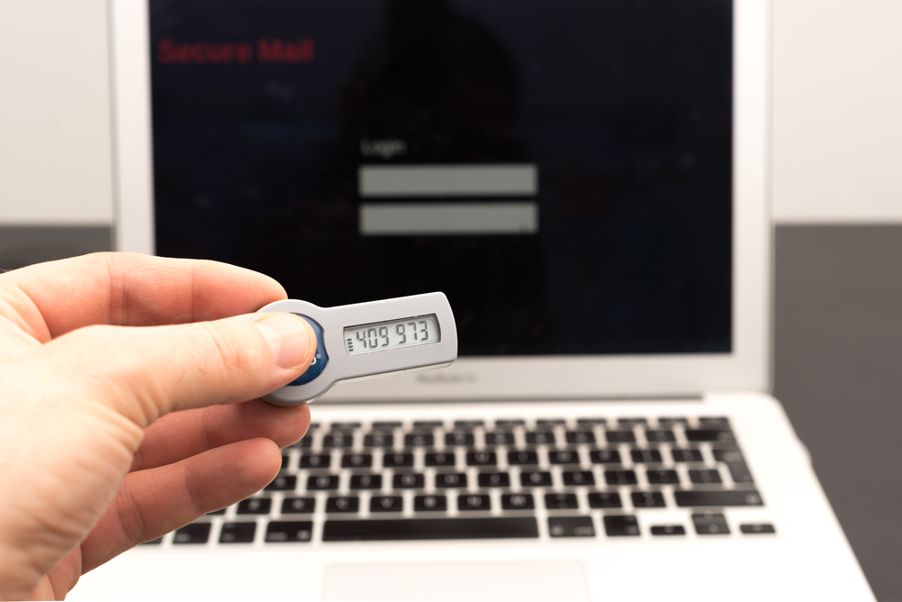 Man's hand holding a secure token in front of a laptop and logs in securely online
