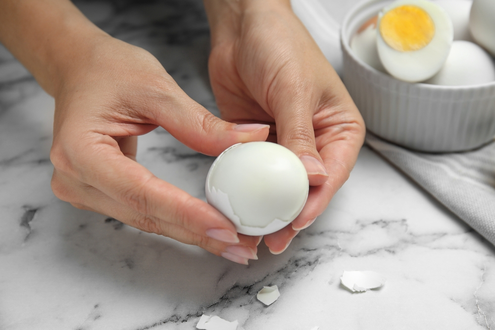 Woman peeling boiled egg at white marble table